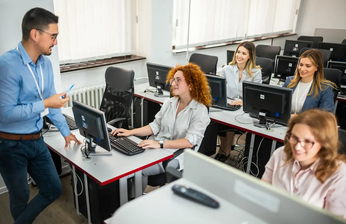 insegnante con studenti seduti al banco con il computer che spiega la lezione di informatica